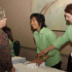 Group interaction: woman in green shirt handing documents to seated attendees at a table; collaborative setting