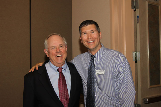 Two men posing: older man in suit with younger man in striped shirt, arm around shoulder