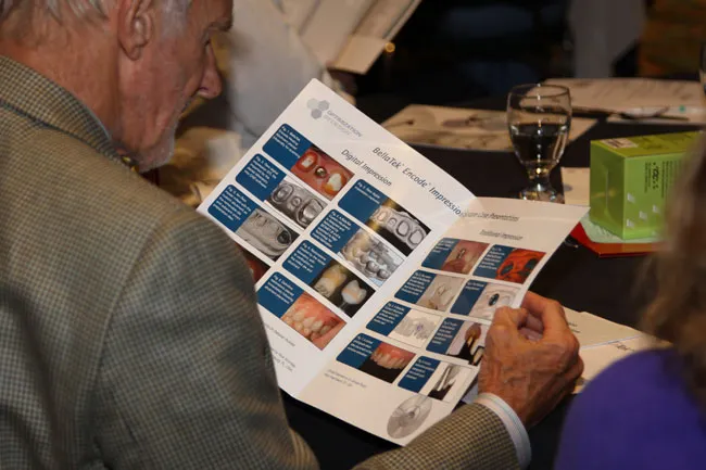 Attendee reviewing open brochure with dental/medical images; glass of water and notebook nearby