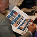 Attendee reviewing open brochure with dental/medical images; glass of water and notebook nearby